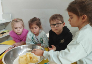 Na zdjęciu widzimy dziewczynkę, która ma na łyżce odmierzoną ilość proszku do pieczenia. Dziewczynka wsypuje składnik do miski.