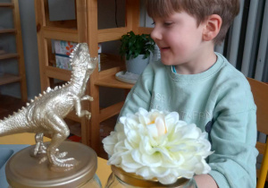 chłopiec siedzi, przed nim stoją słoiki z dinozaurem i kwiatkiem