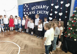 dzieci stoją przed napisem :Kochamy Was całym sercem"