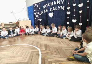 dzieci siedzą przed napisem "Kochamy Was całym sercem"