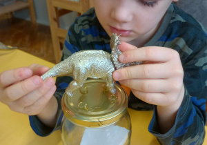 chłopiec przykleja dinozaura do pokrywki od słoika