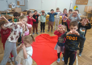 dzieci stoją dookoła serca i robią z rączek serduszka
