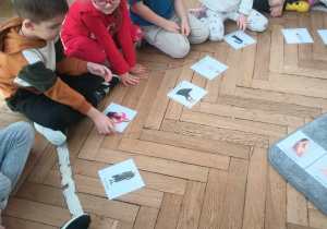 dzieci siedzą na podłodze, przed nimi leżą zdjęcia człowieka