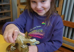 dziewczynka przykleja dinozaura do pokrywki od słoika