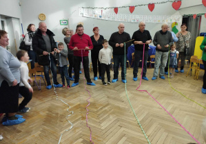 Na zdjęciu widzimy dziadków, którzy biorą udział w konkursie na jak najszybsze zwijanie tasiemki na kij.