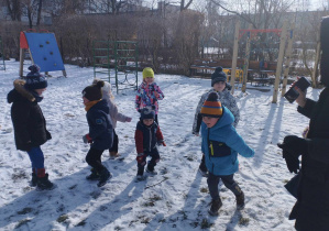 Na zdjęciu widzimy grupkę dzieci, które tańczą do muzyki. obok tańczących dzieci widzimy nauczyciela, który puszcza muzykę z telefonu.