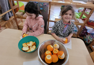 Zdjęcie przedstawia dziewczyni obierające pomarańcze ze skóry.