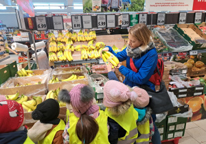 Zdjęcie przedstawia odobe dorosłaą pokazująca dzieciom symbol produkcji ekologicznej.