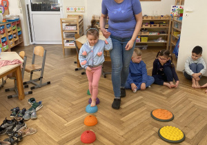 Zdjęcie przedstawia kobietę prowadzącą za rękę dziewczynkę przez ścieżkę sensoryczną.