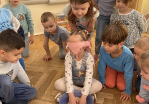 Zdjęcie przedstawia dziewczynkę z zasłoniętymi oczami, która wkłada ręce do miski z fasolą.