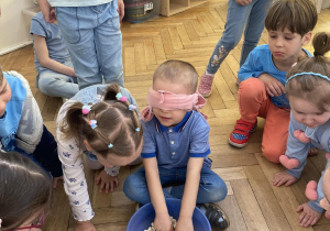 Zdjęcie przedstawia chłopca z zasłoniętymi oczami, który wkłada ręce do miski z fasolą