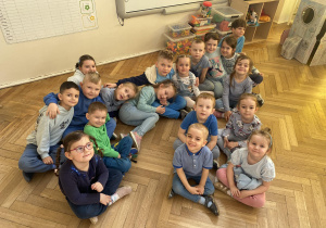 Zdjęcie przedstawia dzieci w niebieskich koszulkach, siedzących w grupie na podłodze.
