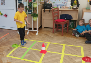Chłopiec niesie na łyżce piłeczkę pinpongową.