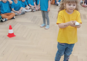 Dziewczynka trzyma na łyżce piłeczkę pinpogową.