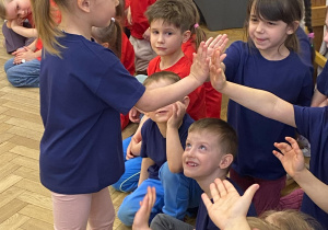 Zdjęcie przedstawia dziewczynkę przebijającą "piątkę" z kolegami z grupy.