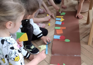 dzieci przyklejają figury geometryczne na papier, tworzą wspólną pracę