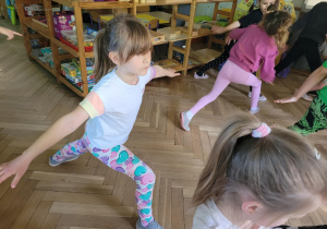 Zdjęcie przedstawia dzieci wykonujące ćwiczenia ruchowe z elementami jogi.