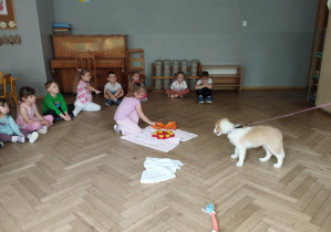 Na zdjęciu widzimy dziewczynkę, która wkłada smaczka do maty edukacyjnej dla piesków. Bibi obserwuje.
