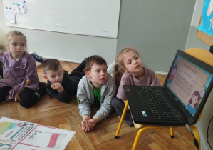 Na zdjęciu widzimy grupkę dzieci, które oglądają film edukacyjny dotyczący zbliżających się świąt majowych.