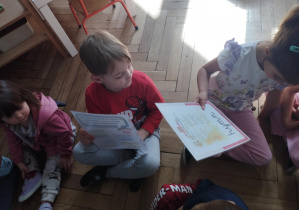Na zdjęciu widzimy dzieci, które oglądają ilustracje przedstawiające hymn i walutę Polski.
