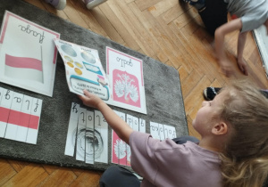 Na zdjęciu widzimy dziewczynkę, która przyporządkowuje do ułożonych puzzli ilustrację przedstawiającą walutę Polski.