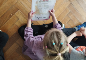 Na zdjęciu widzimy dziewczynkę, która ogląda ilustrację przedstawiającą hymn Polski.