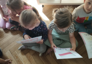 Na zdjęciu widzimy dzieci, które oglądają ilustracje przedstawiające flagę, hymn i godło Polski.