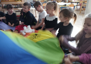 Na zdjęciu widzimy dzieci, które uczestniczą w zabawie z wykorzystaniem chusty animacyjnej i koni.