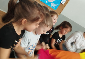 Na zdjęciu widzimy dzieci, które uczestniczą w zabawie z wykorzystaniem chusty animacyjnej i koni.