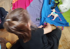Na zdjęciu widzimy dziewczynkę, która chowa pod chustę animacyjną figurkę konika.