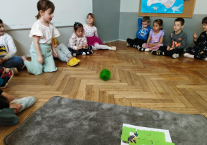 Na zdjęciu widzimy dziewczynkę, która rzuca kostą. Wylosowaną cyfrę musi odnależć na ilustracji umieszczonej na dywaniku i odkryć ją.