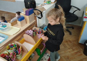 Na zdjęciu widzimy dziewczynkę, która szuka kartki z małym motylem umieszczonym w klasie.
