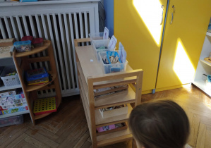 Na zdjęciu wdizimy dziewczynkę, która na szafce z działu językowego szuka ukrytej ilustracji motyla.