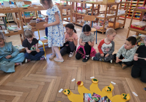Zdjęcie przedstawia dzieci siedzące w kręgu na podłodze.