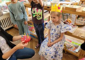 Zdjęcie przedstawia solenizantkę siedząca na i przed nią kucająca nauczycielke, która trzyma w tęku tort ze świeczkami.