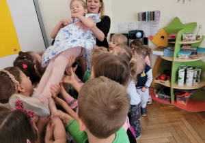 Zdjęcie przedstawia nauczycielkę i dzieci trzy,ające solenizantkę.