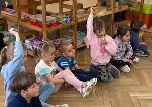 Zdjęcie przedstawia dzieci siedzące obok siebie. Dwoje dzieci zgłasza się do odpowiedzi.