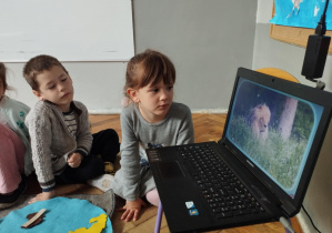 Na zdjęciu widzimy trójkę dzieci, które oglądają film o zwierzętach zamieszkujących Afrykę.