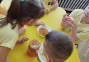Na zdjęciu widzimy dziewczynkę, która chce powąchać miodu w miseczce.
