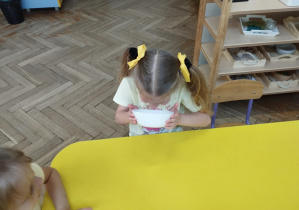 Na zdjęciu widzimy dziewczynkę, która wącha miód w miseczce.