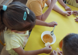 Na zdjęciu widzimy dziewczynkę, która nalewa sobie na wafelek odrobinę miodu do skosztowania.