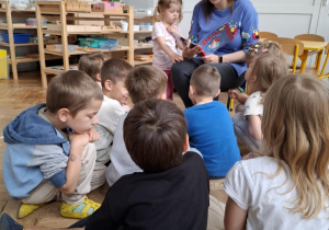 kobieta trzyma w rękach książkę, przed nią siedzą dzieci