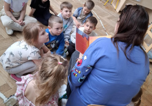 grupa dzieci patrzy na kobietę, która czyta im książkę