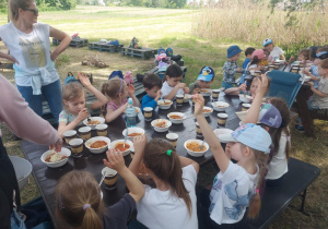 Grupa dzieci jedząca spagetti przygotowane samodzielnie i ugotowane na ognisku