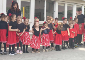 Zdjęcie przedstawia dzieci i nauczycielkę stojących na tarasie. Wszyscy mają czarno- czerwone stroje.