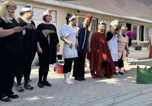 Zdjęcie przedstawia pracowników przedszkola ustawionych w rzędzie. Są oni przebrani w stroje do bajki Kaczka dziwaczka.