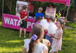 Zdjęcie przedstawia dzieci ustawione w kolejce do waty cukrowej i popcornu.