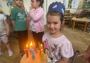 Zdjęcie przedstawia dziewczynkę przy torcie z zapalonymi świeczkami.