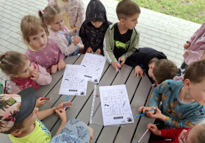 dzieci siedzą przy stoliku w ogrodzie, na stole leżą kartki
