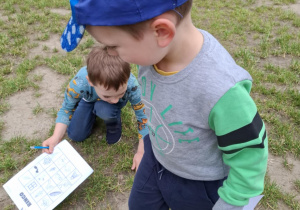 chłopcy szukają na ziemi elemntów, które narysowane są na kartce